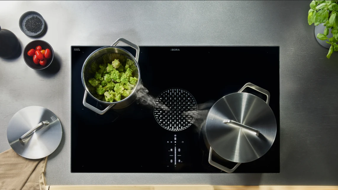 Induction hob with a downdraft extractor drawing steam from a pan
