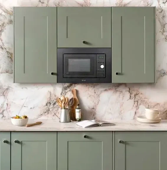 Built-in microwave in sage green cabinetry above a marble splashback