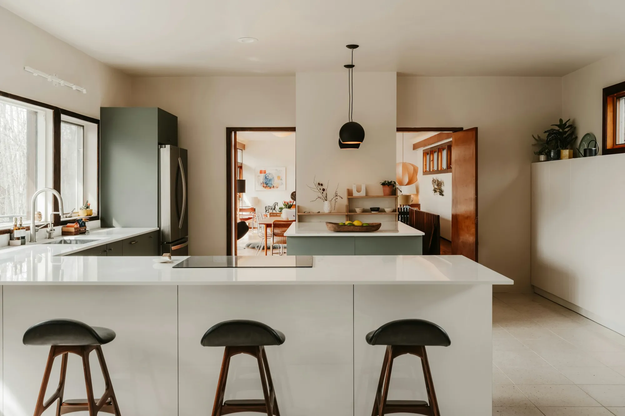Modern kitchen with sage green cabinets, a white island and black bar stools