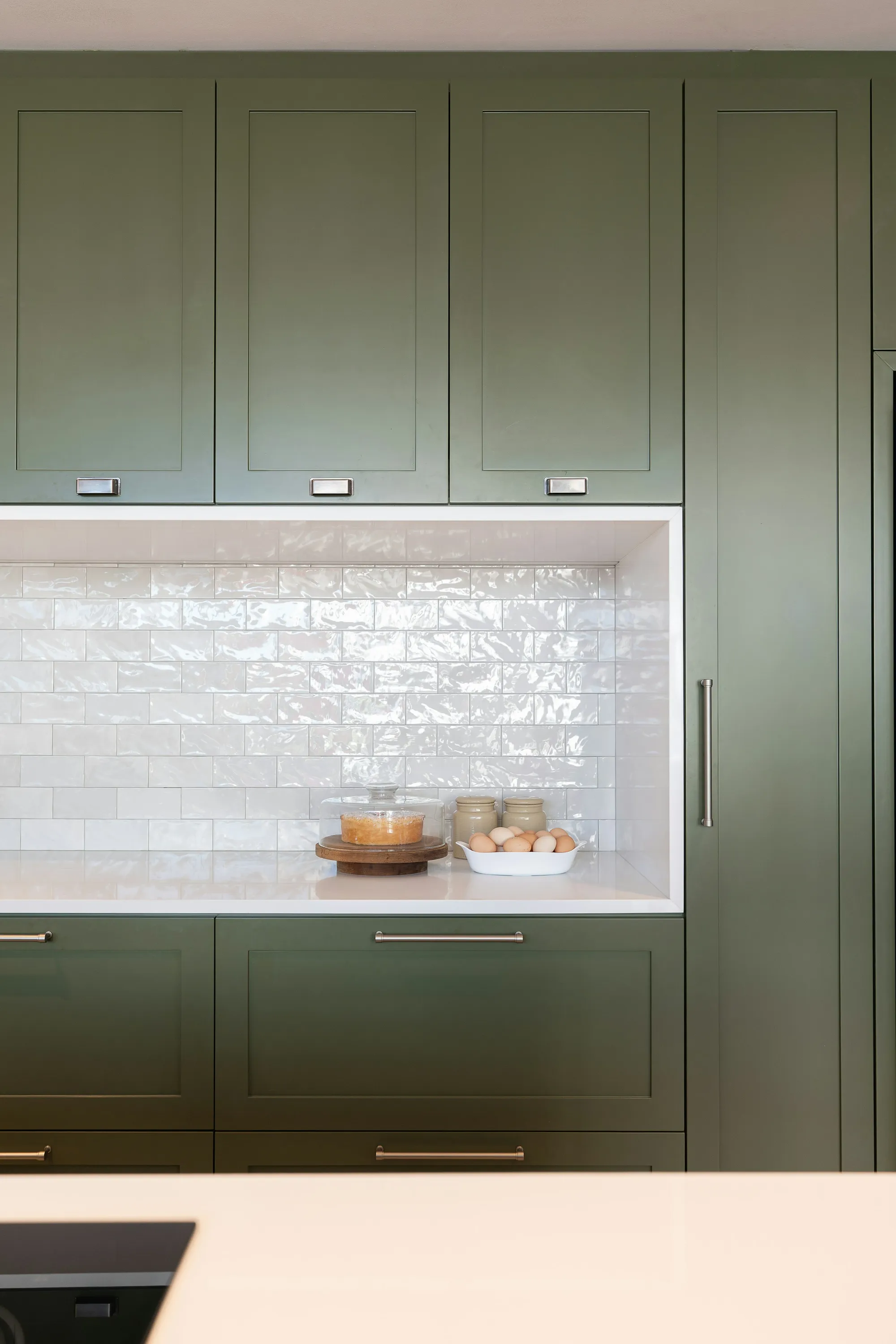 Olive green shaker cabinets beside a white tiled niche