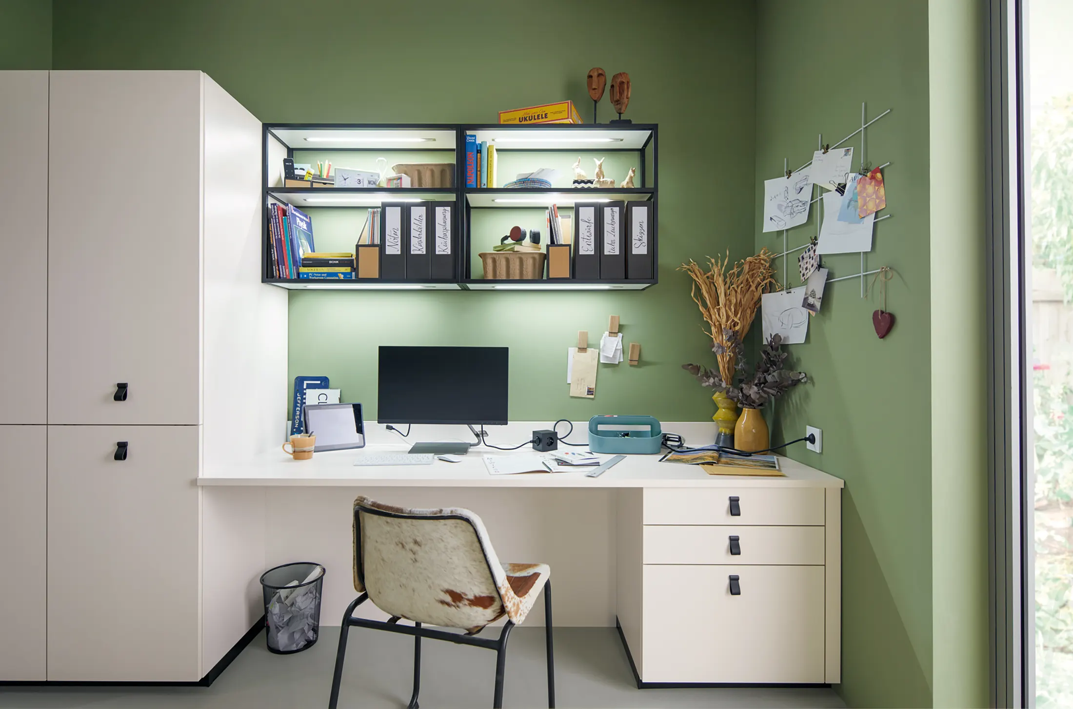 Home office with built-in desk and storage against a green wall