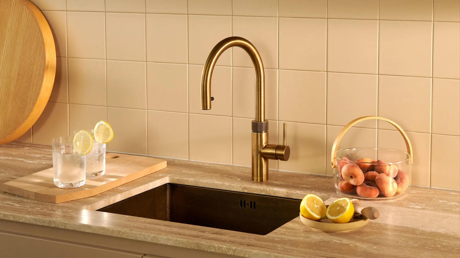 Quooker Flex tap in patinated brass beside an undermount sink, with glasses of sparkling water