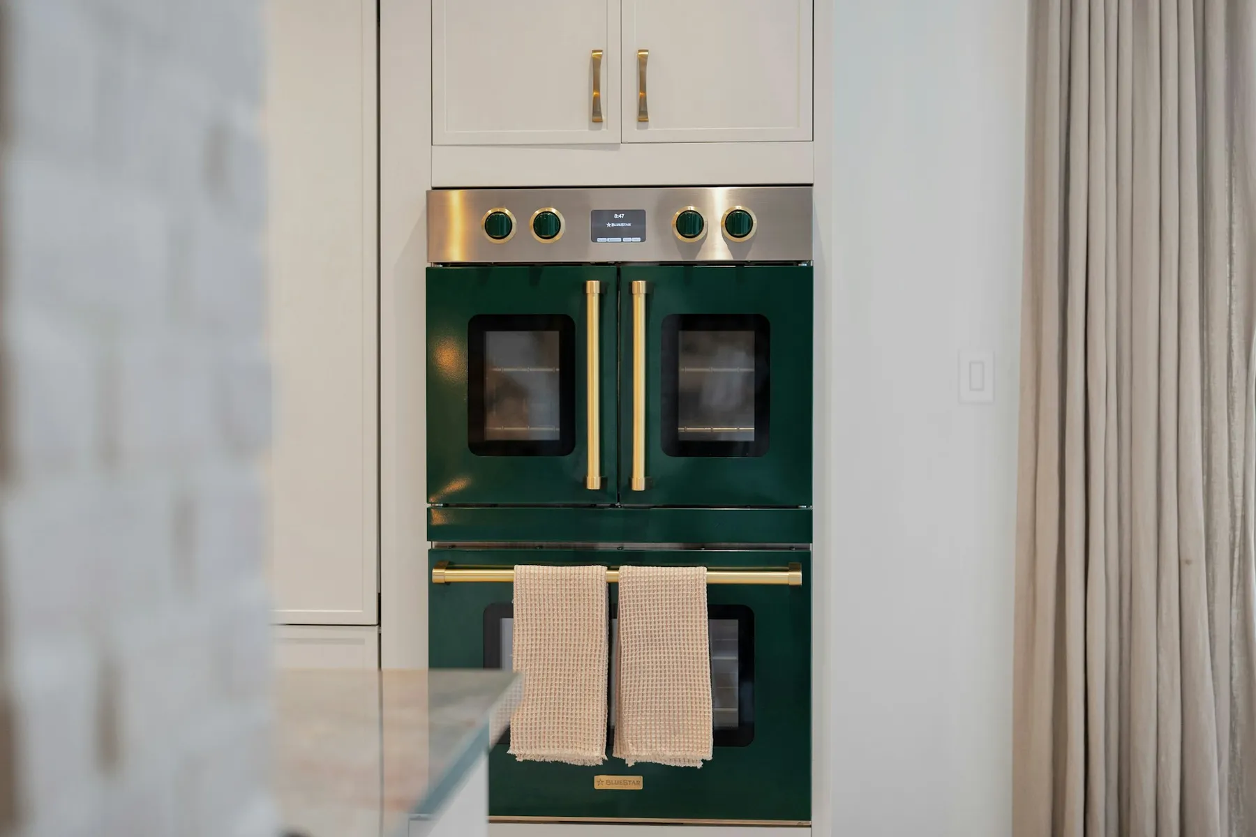 Dark green double oven with brass handles in a bright kitchen